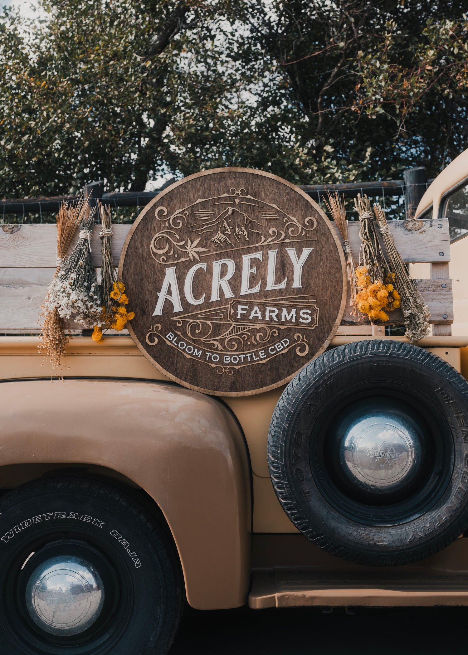 Image of rustic truck with dried flowers hanging down, and large wooden Acrely Farms logo display