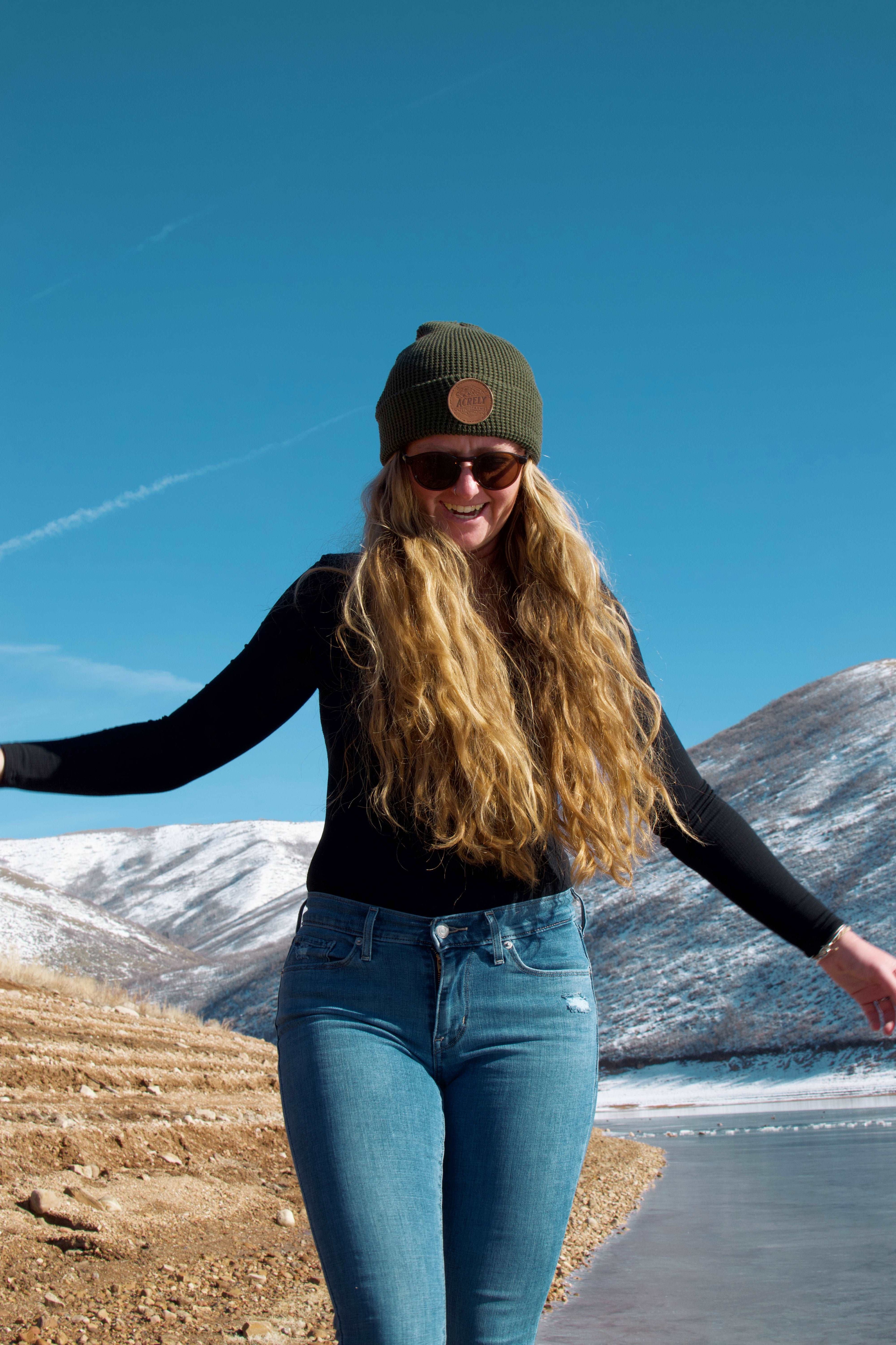 A woman wearing a Waffle Knit Acrely Farms Green Beanie with the mountains in the background