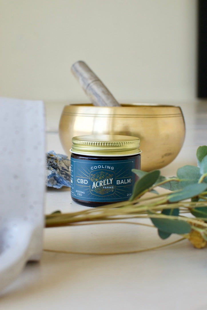 Acrely Farms Cooling CBD Balm on a surface with a mortar and pestle and plant in the background
