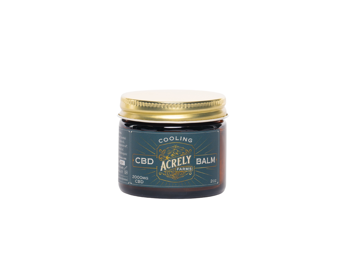 A small amber glass jar of Acrely Farms Cooling CBD Balm with a gold metal lid and a dark teal label, centered on a plain white background.
