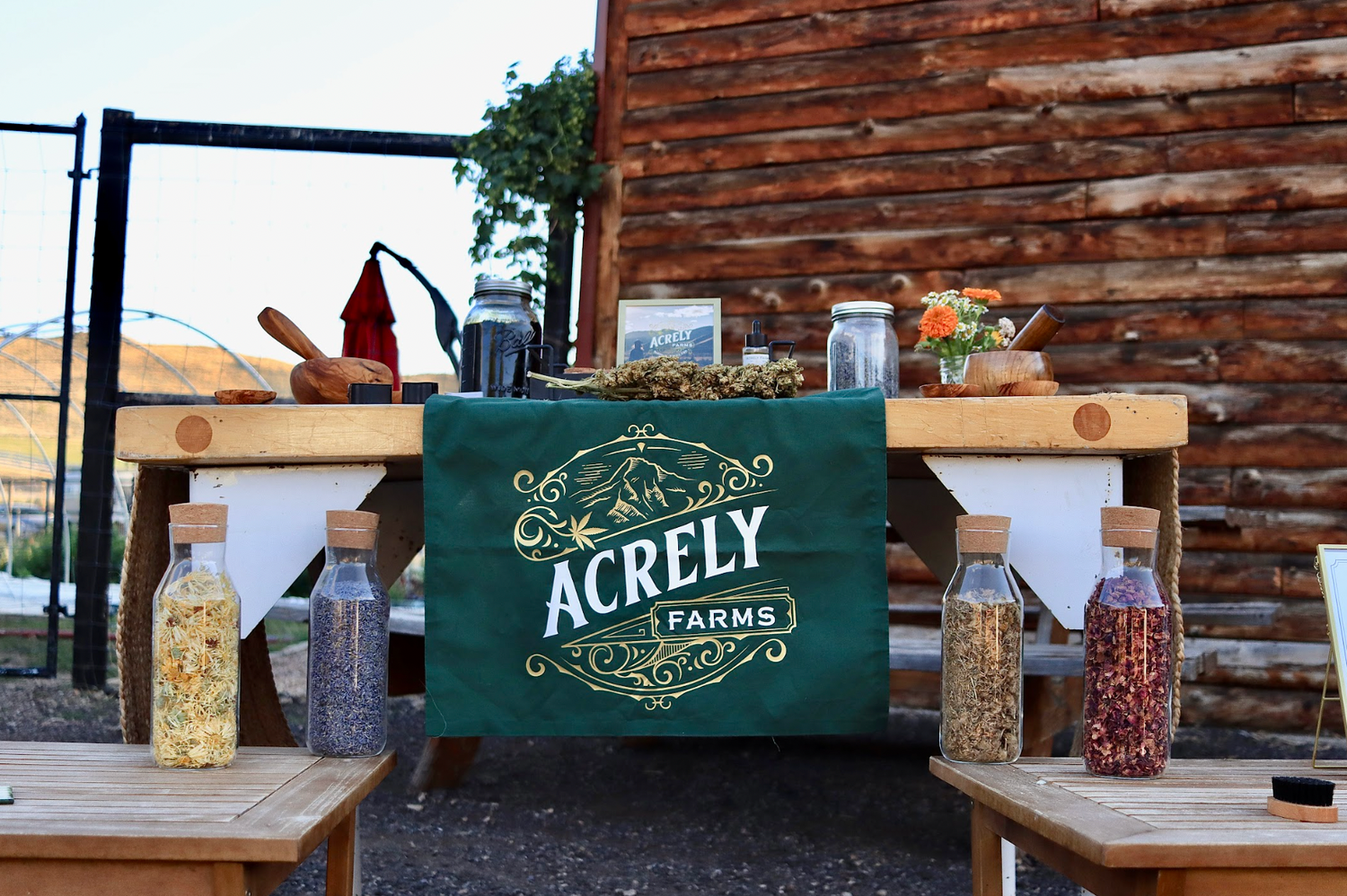 Outdoor setting of Acrely Farms Harvest Retreat education table with branded tablecloth and various items on wooden tables.