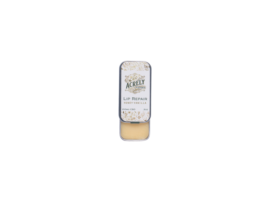 A small rectangular metal tin of Acrely Naturals Lip Repair balm in Honey Vanilla, shown open with the beige balm visible inside, centered on a plain white background.