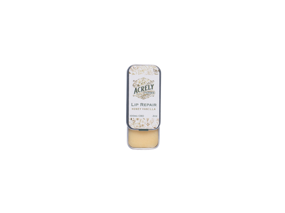 A small rectangular metal tin of Acrely Naturals Lip Repair balm in Honey Vanilla, shown open with the beige balm visible inside, centered on a plain white background.