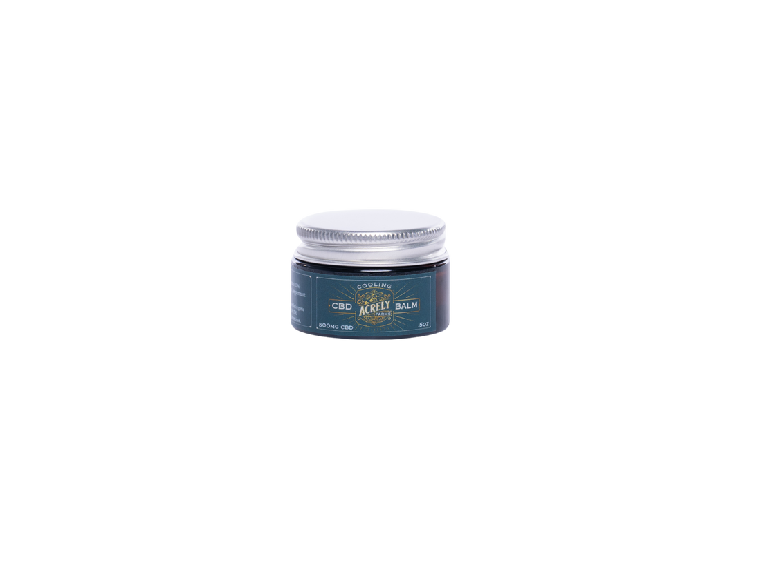 A small jar of CBD Cooling Balm with a dark teal label and a silver metal lid, centered on a solid white background.