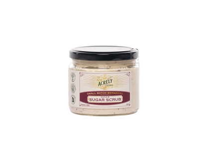 A jar of Acrely Farms Small Batch Sugar Scrub, featuring a beige scrub inside a clear glass jar with a black lid and a cream-colored label.