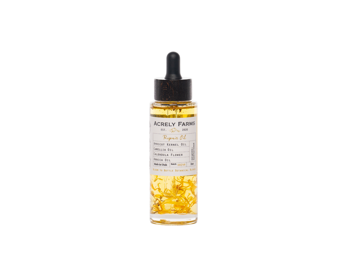 A clear glass dropper bottle of Acrely Farms Repair Oil with a black rubber dropper cap, filled with golden-yellow oil and containing visible dried yellow flower petals, set against a plain white background.