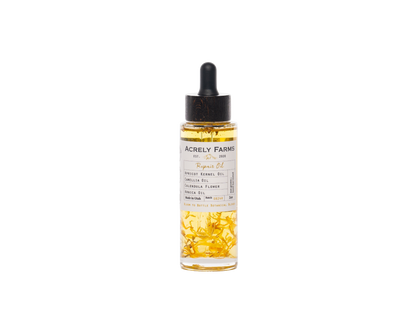 A clear glass dropper bottle of Acrely Farms Repair Oil with a black rubber dropper cap, filled with golden-yellow oil and containing visible dried yellow flower petals, set against a plain white background.