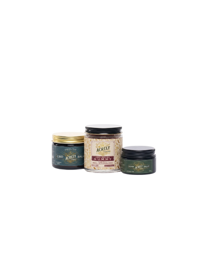 Three jars of Acxióy hair products arranged together on a plain white background, including a dark green jar with a gold lid, a clear jar filled with beige strands, and a dark green jar with a black lid.